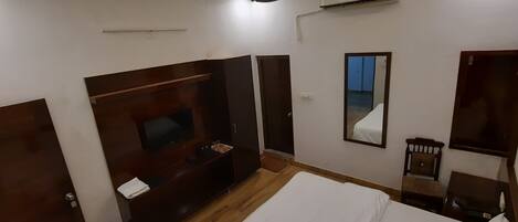 Un dormitorio con cama, televisión, armario, espejo y aire acondicionado.
