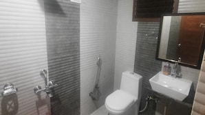 A bathroom with a toilet, sink, shower, and a mirror.