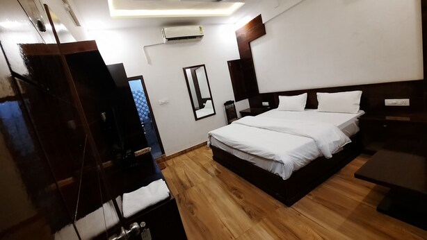 A modern hotel room with a wooden floor, a large bed with white linens, a ceiling fan, and an air conditioning unit.