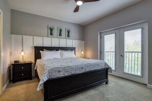 Un dormitorio con cama, mesitas de noche, ventilador de techo y vistas a través de una puerta.