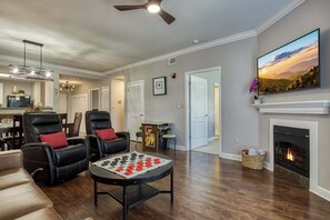 Una sala de estar con chimenea, televisor montado encima y una mesa de ajedrez.