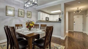 A dining area with a wooden table set for six, surrounded by chairs, and a chandelier above. - Mountain View Condo by Beyond Expectations: 2BR w/ Pools, Balcony & King Beds (Pigeon Forge)