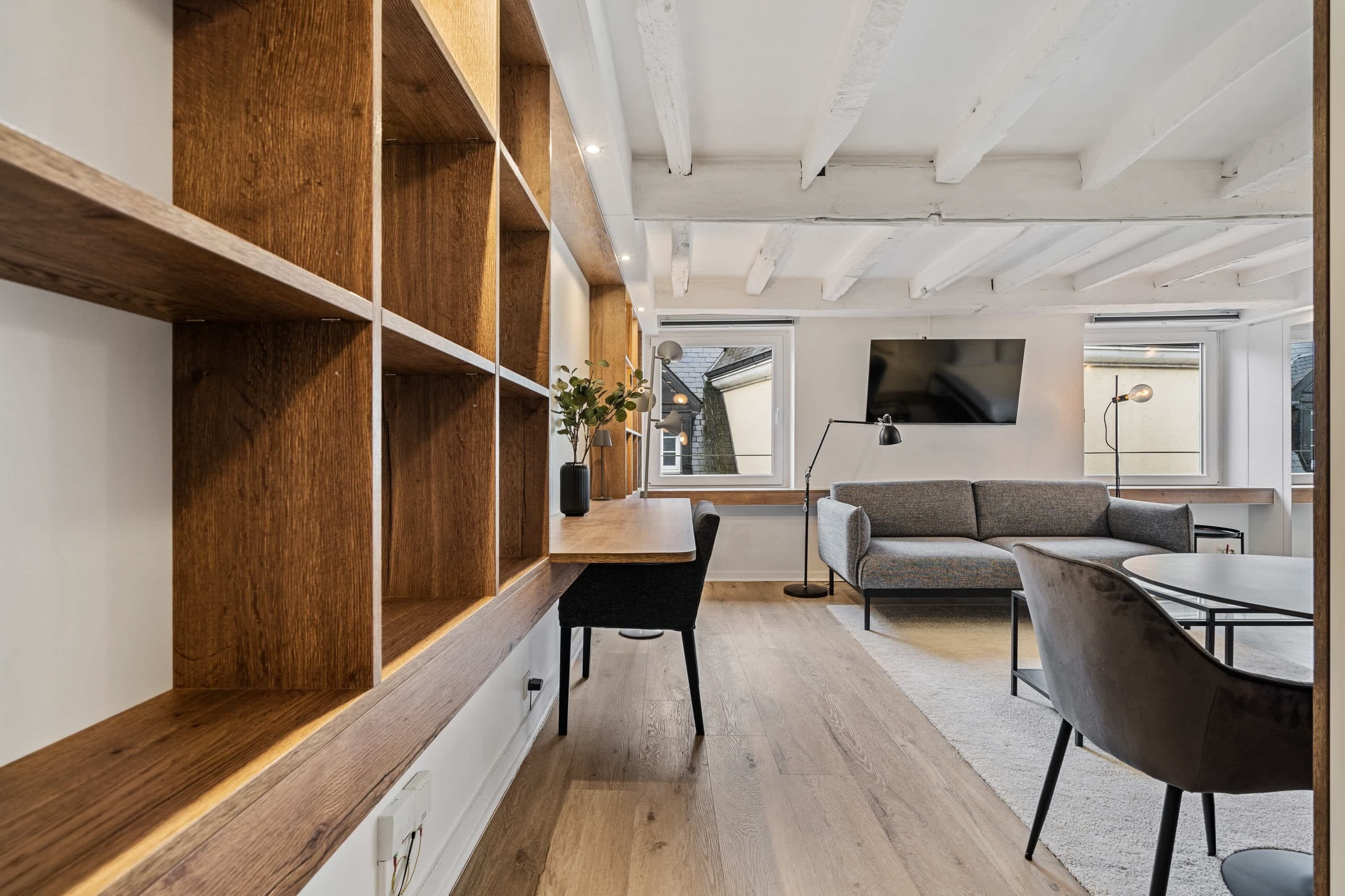 A modern interior with wooden shelves, a dining table, a sofa, and a TV mounted on the wall.