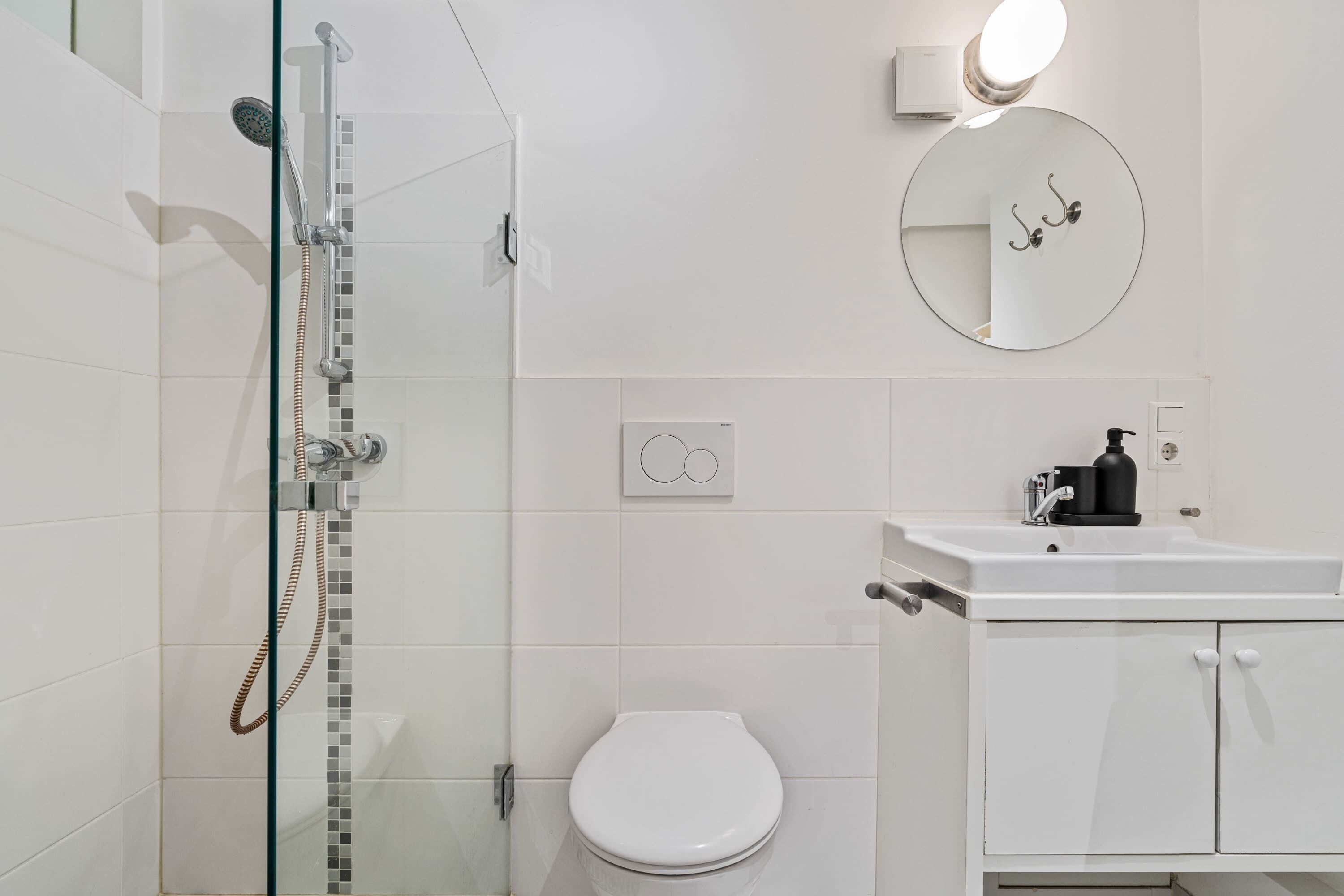Een moderne badkamer met een glazen douchecabine, een wit toilet en een wastafel met een zwarte zeepdispenser.