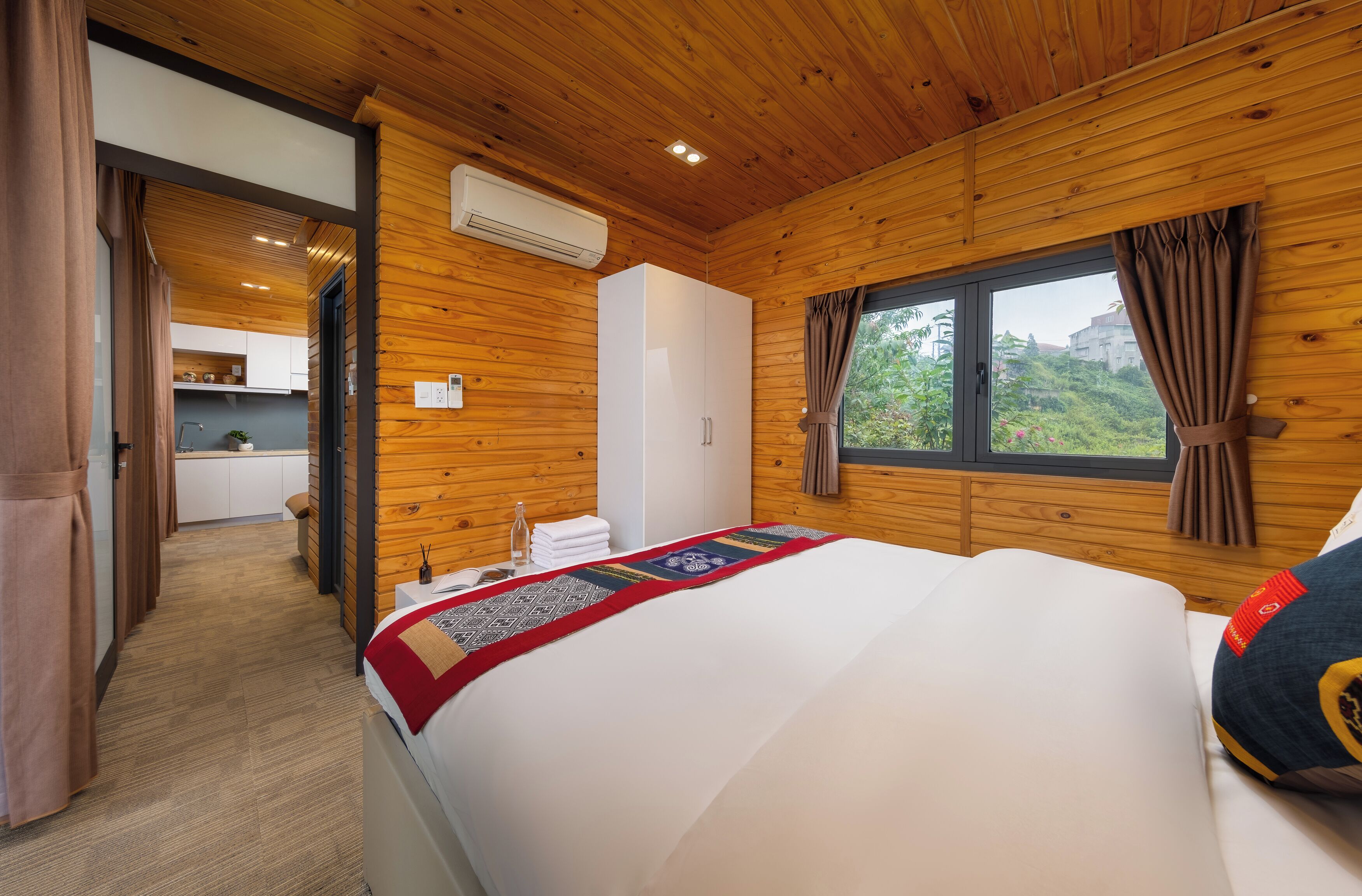 A wooden-paneled room with a bed, a window with curtains, and a view of greenery outside.