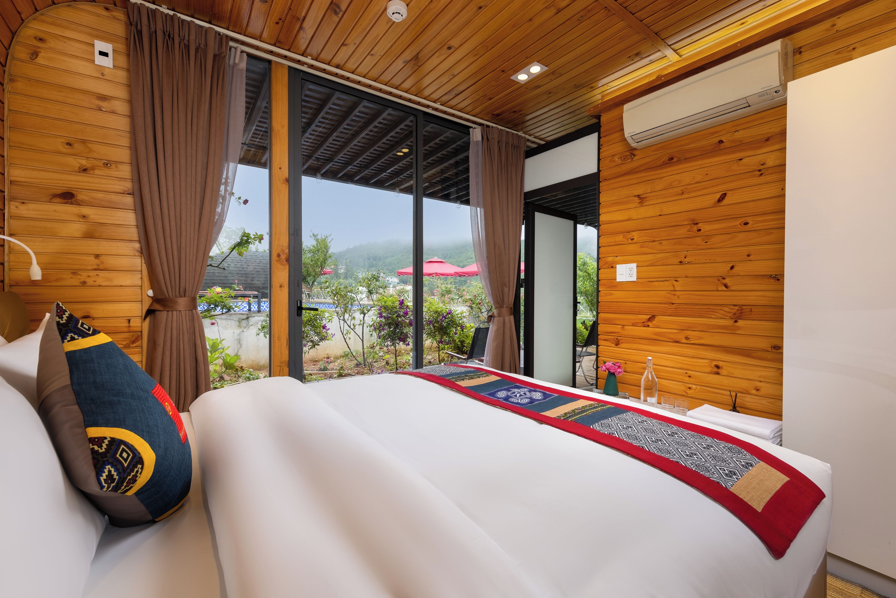 A hotel room with a large bed, wooden walls, a view of the outdoors, and a window with curtains.