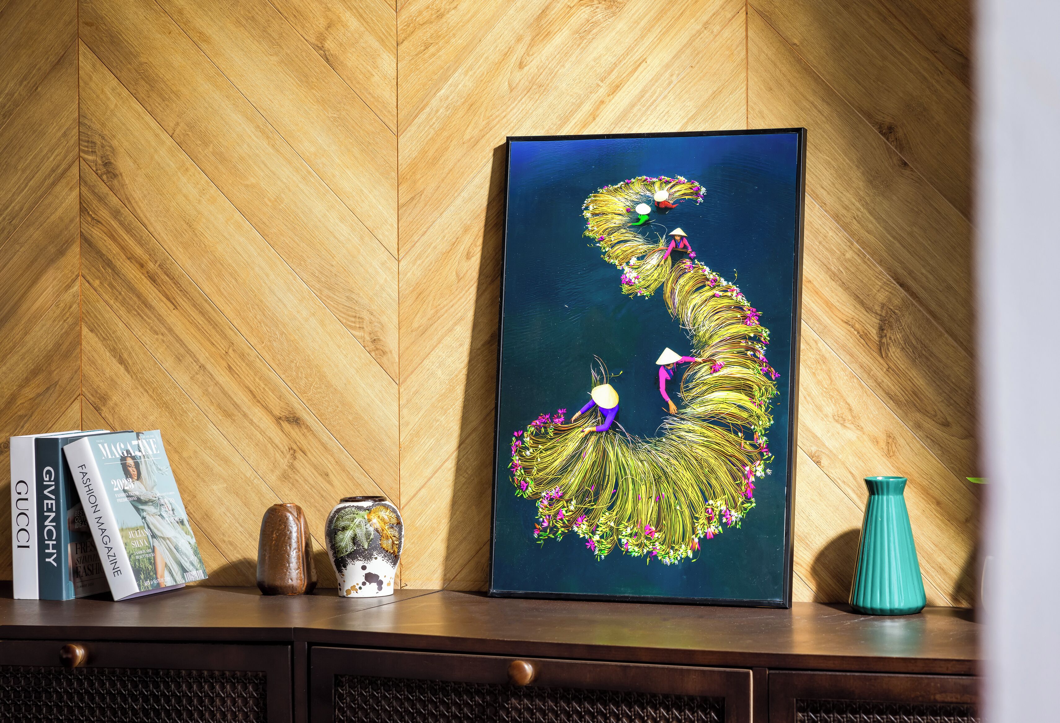 A framed artwork on a wooden wall, a magazine, a ceramic vase, and a small sculpture on a wooden shelf.