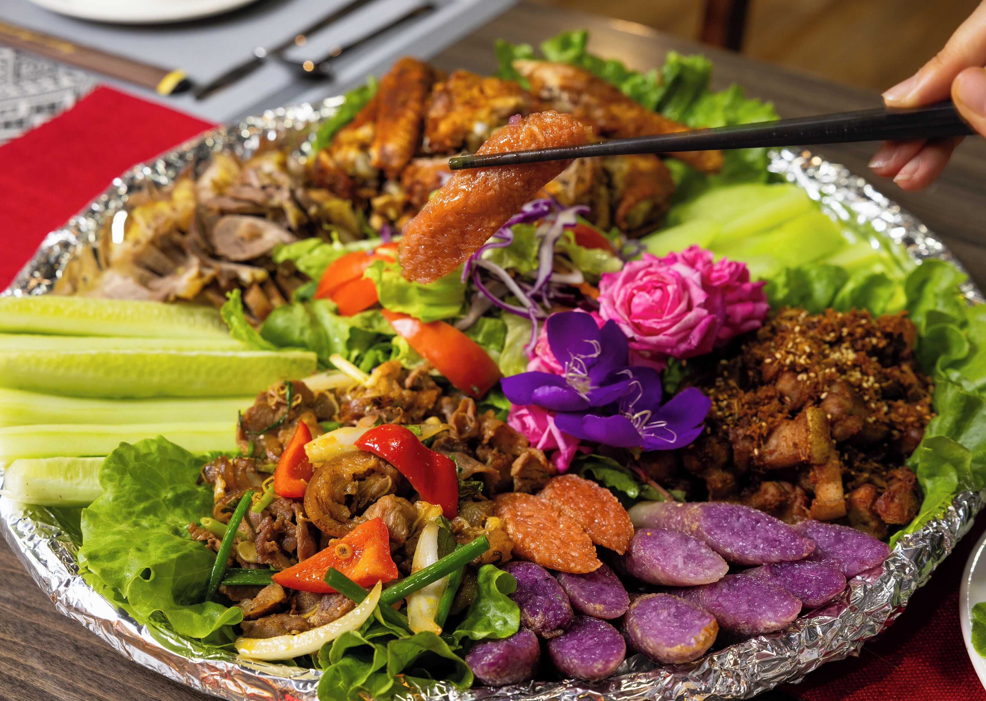 A meal with various dishes including meat, vegetables, and purple-colored items, served on a foil-covered tray.