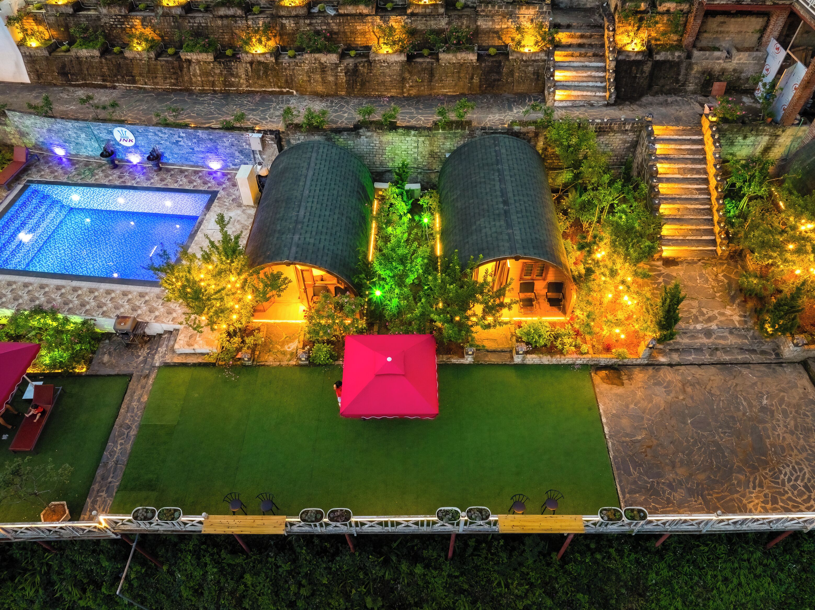 A rooftop pool area with a hot tub, a small deck with chairs, and a red umbrella.