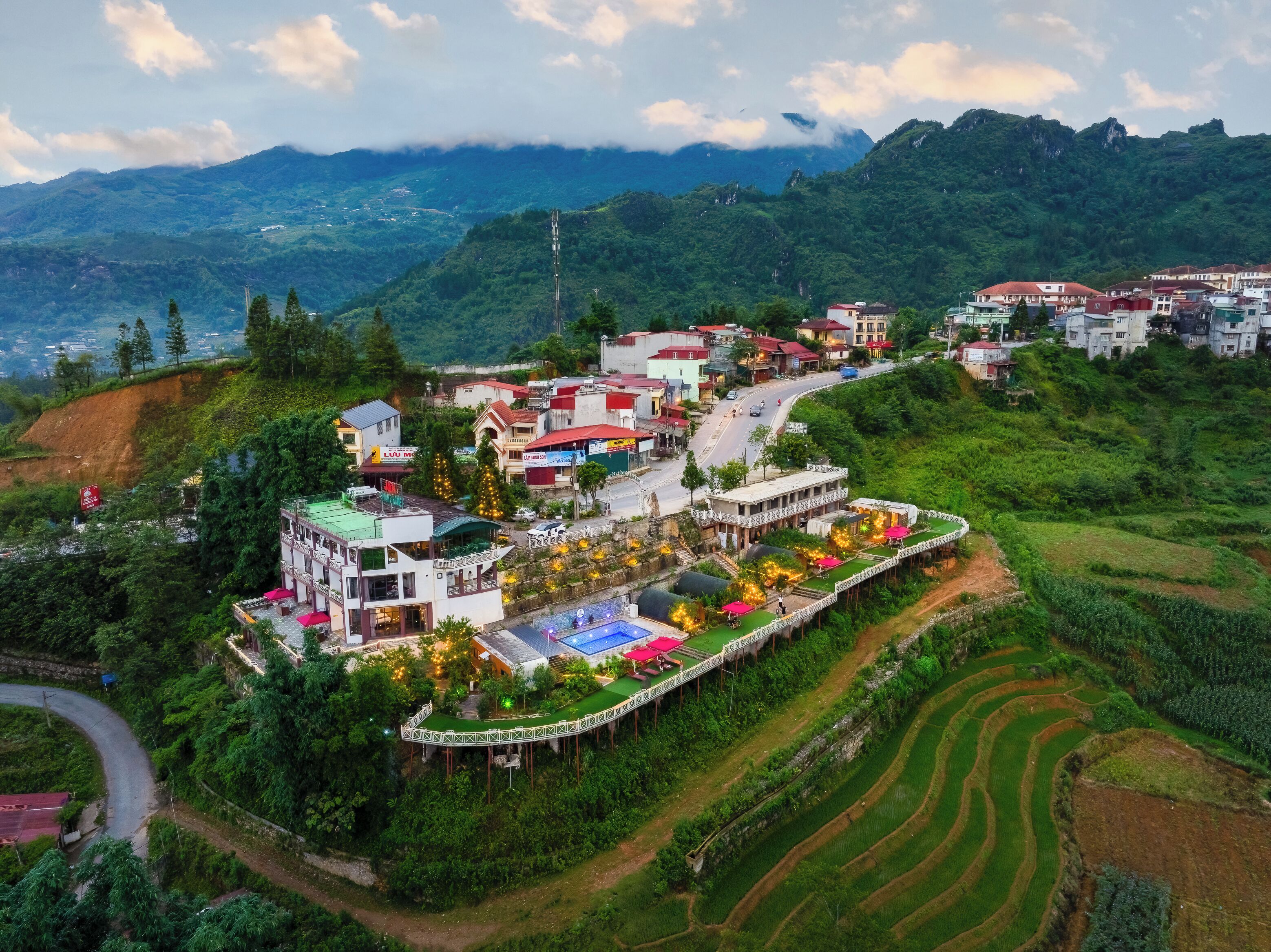 A hillside village with terraced fields, a winding road, and buildings with red roofs.