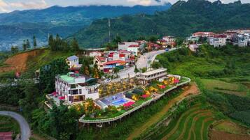 A hillside village with terraced fields, a winding road, and buildings with red roofs.