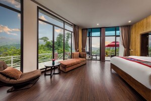 Una habitación de hotel moderna con una cama grande, un sofá, una mesita y un balcón con vistas al paisaje.