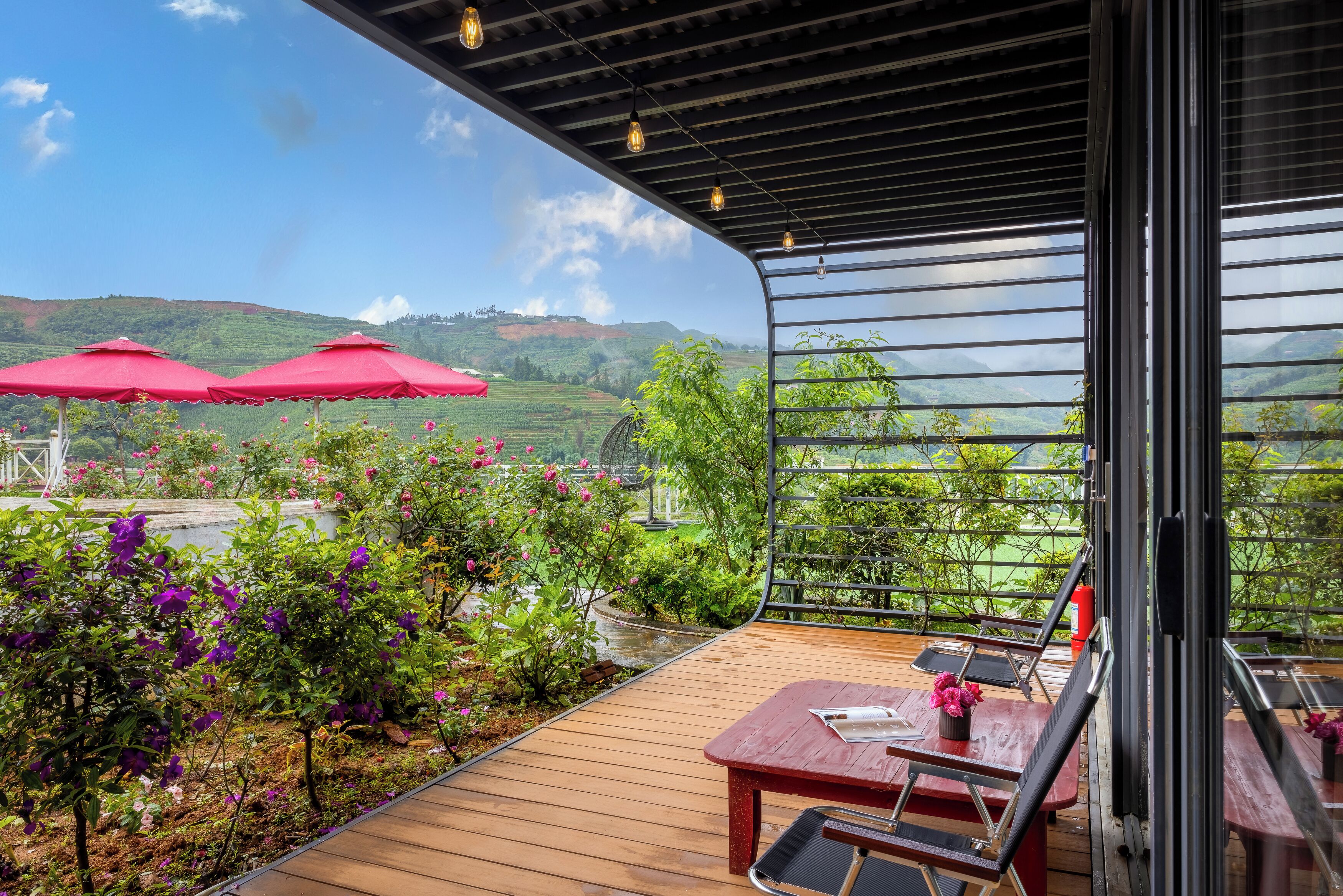 Una terraza con suelo de madera, sombrillas rojas y vistas a colinas verdes.