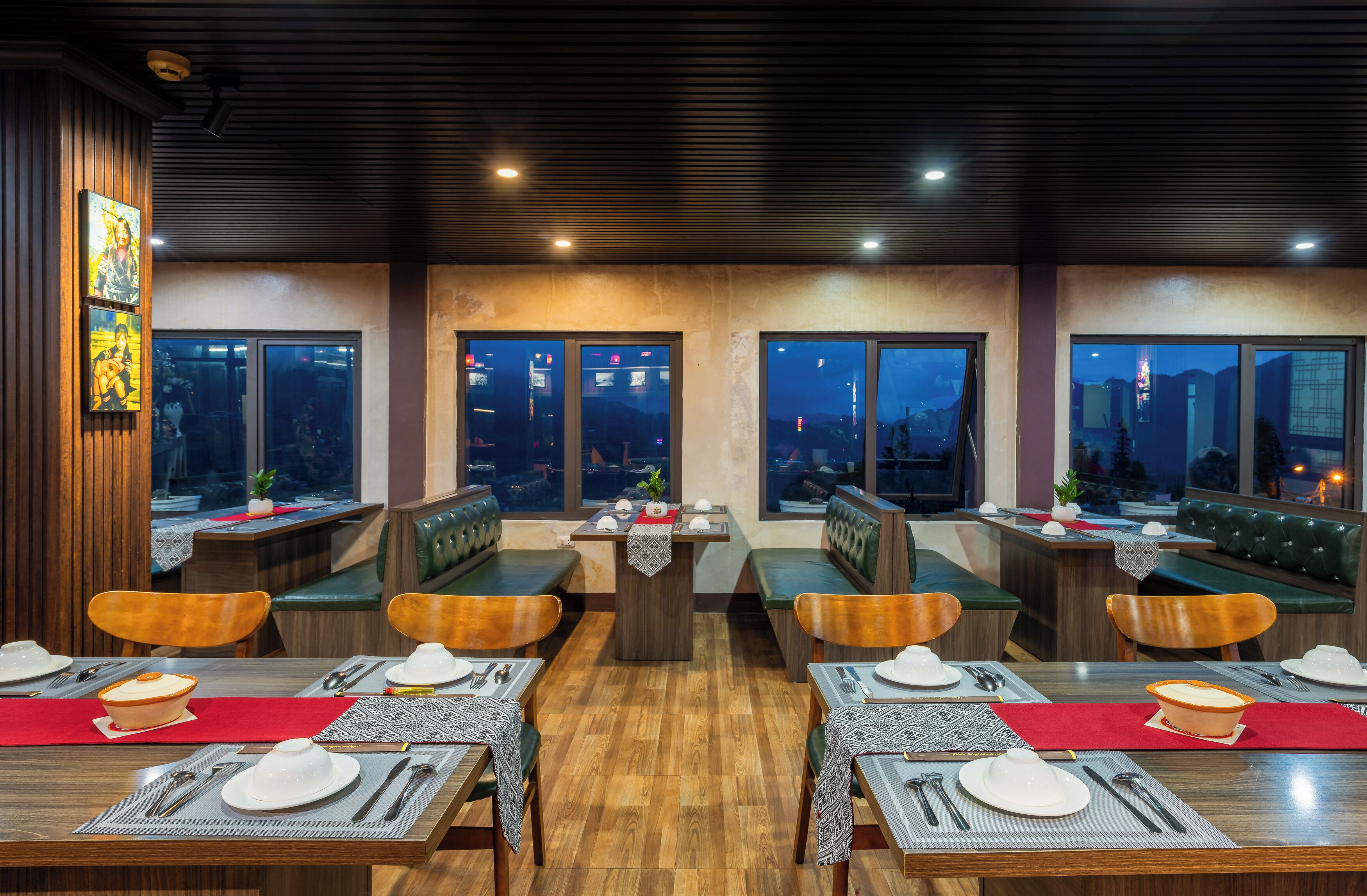 A restaurant with wooden tables and green cushioned booths, arranged in a U-shape with large windows offering city views.