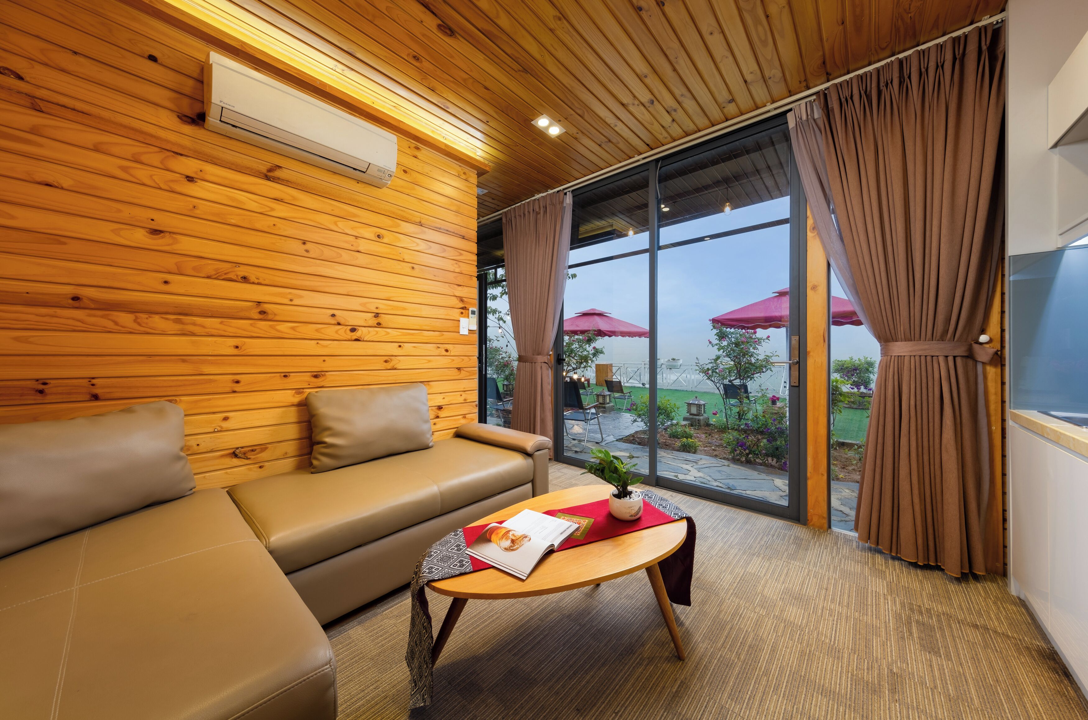 A modern room with a wooden ceiling, a leather sofa, a wooden coffee table with a magazine, and a large window with curtains.
