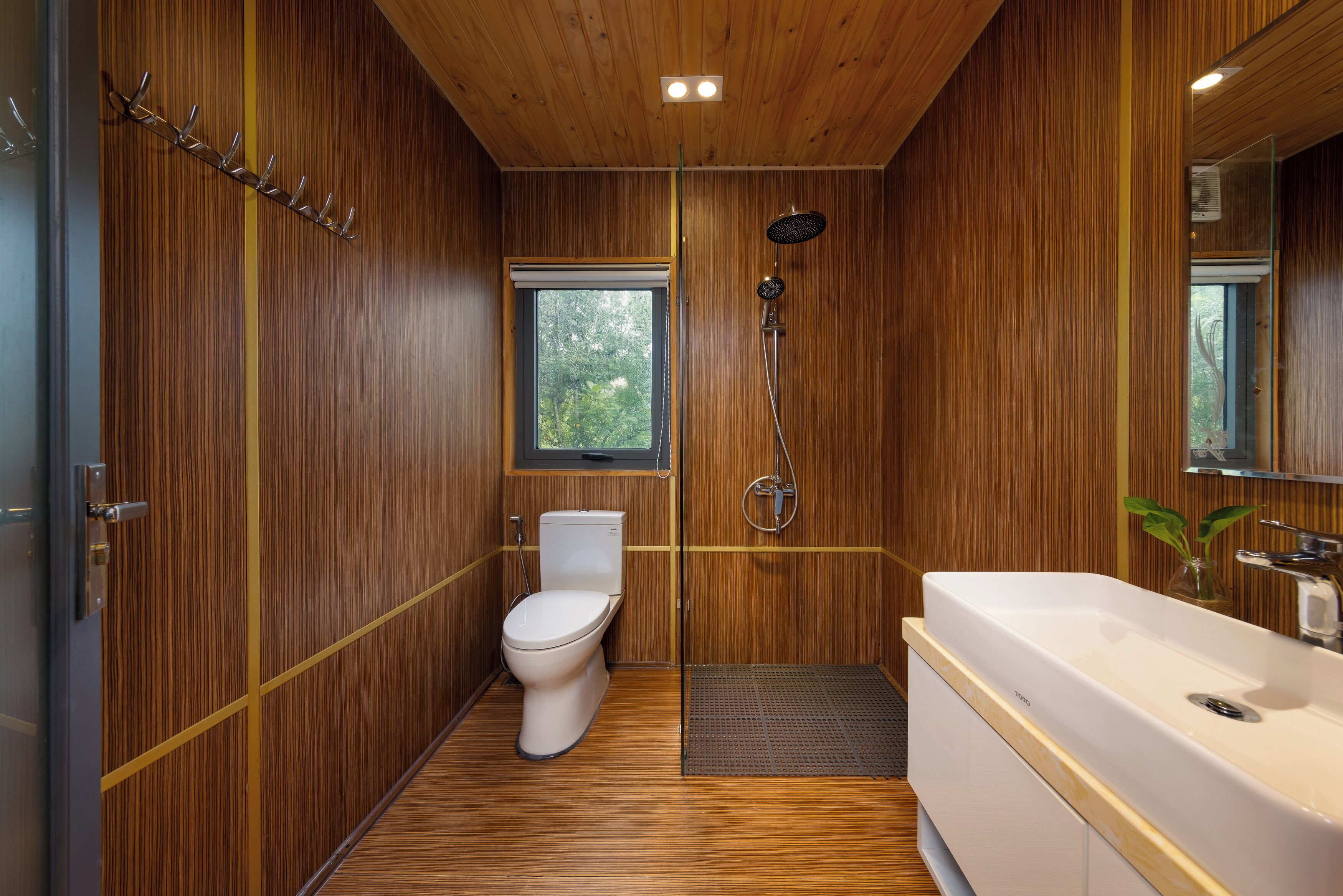A modern bathroom with wooden paneling, a toilet, a shower, and a large bathtub.