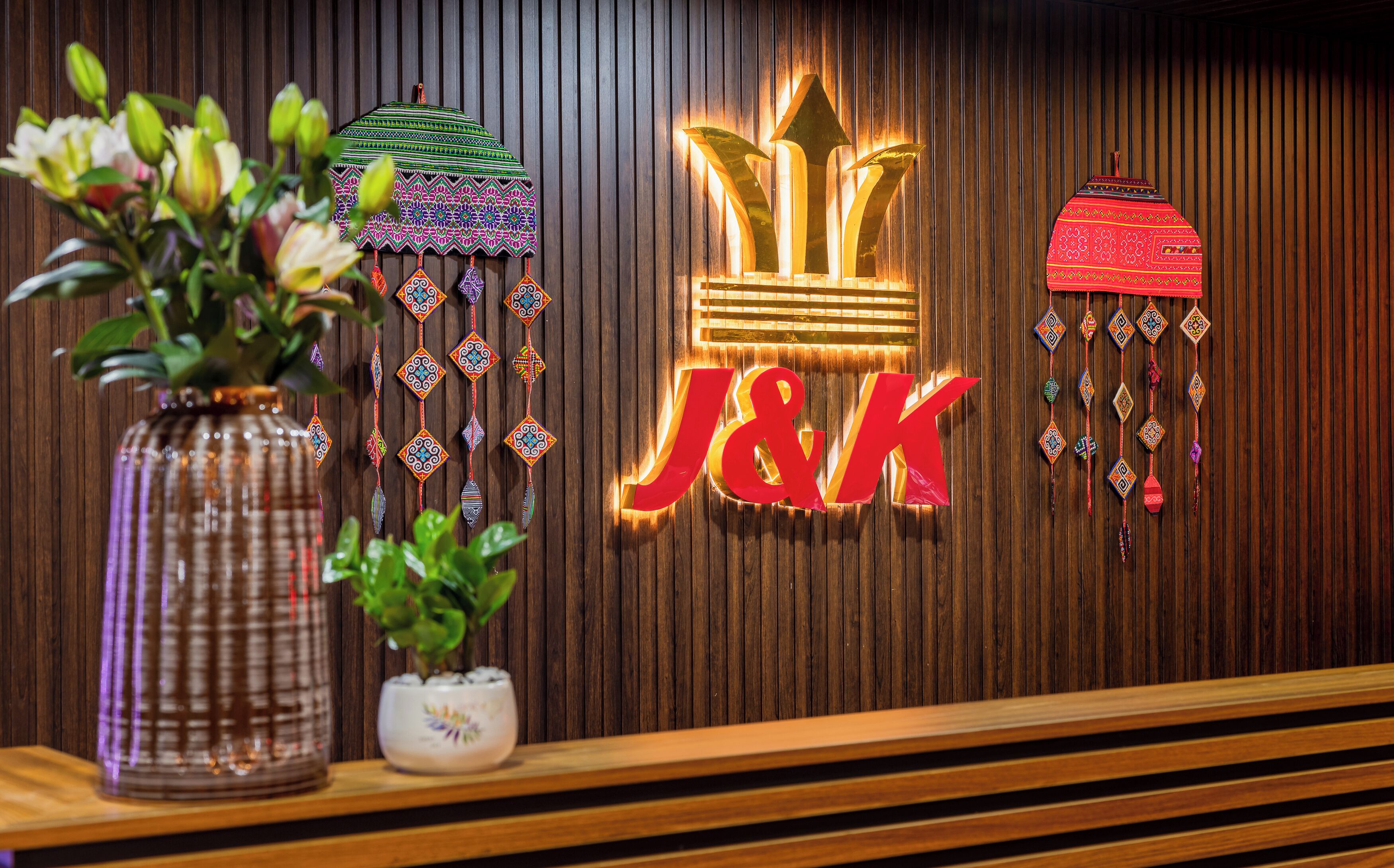 A reception desk with a wooden panel background, a vase with flowers, and decorative hanging ornaments.