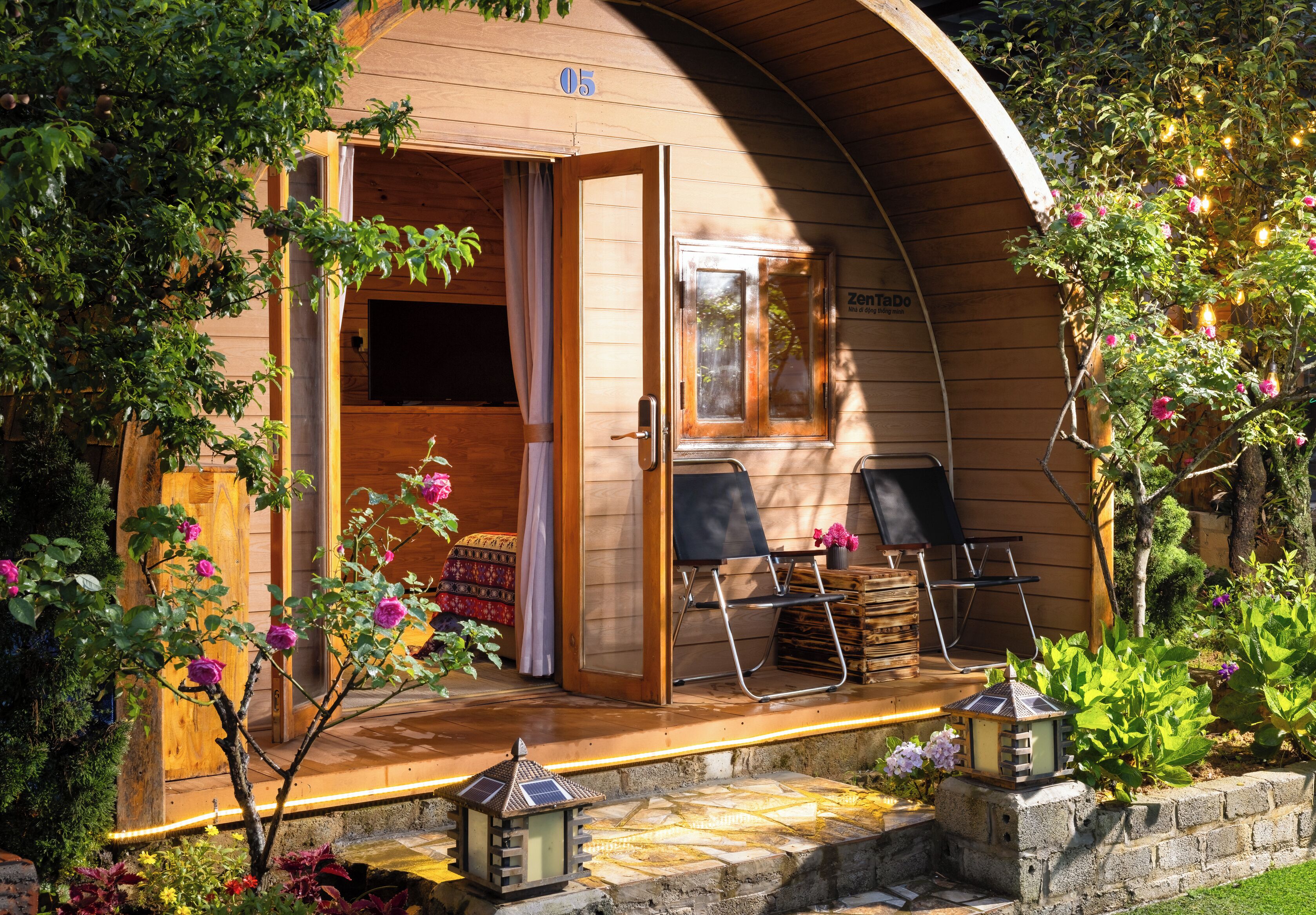 A wooden cabin with a porch, a door, and a window. There are chairs and a table on the porch.
