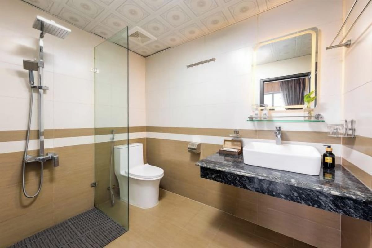 A modern bathroom with a glass shower enclosure, a white toilet, a marble sink, and a large mirror with a lighted frame.
