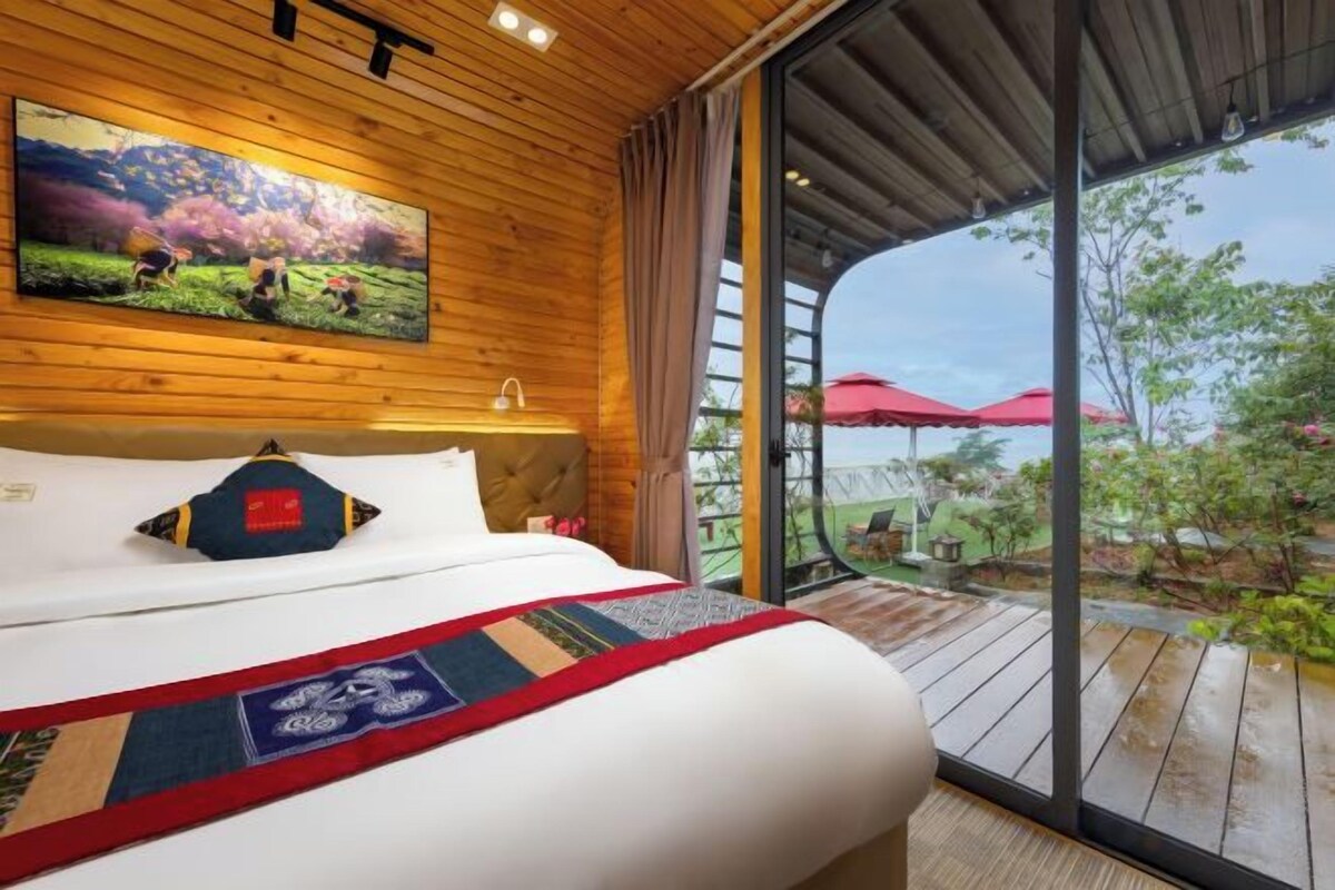 A hotel room with a large bed, a television mounted on the wall, and a view of the outdoors through a sliding glass door.