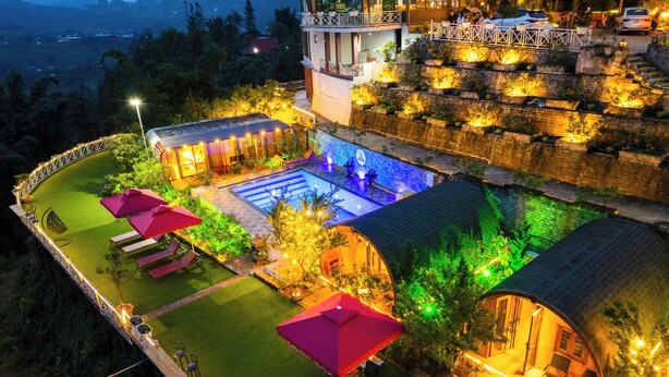 A rooftop pool area with multiple lounge chairs and umbrellas, surrounded by lush greenery and stone walls. - JK Sapa Homestay & Swimming Pool (Sa Pa)