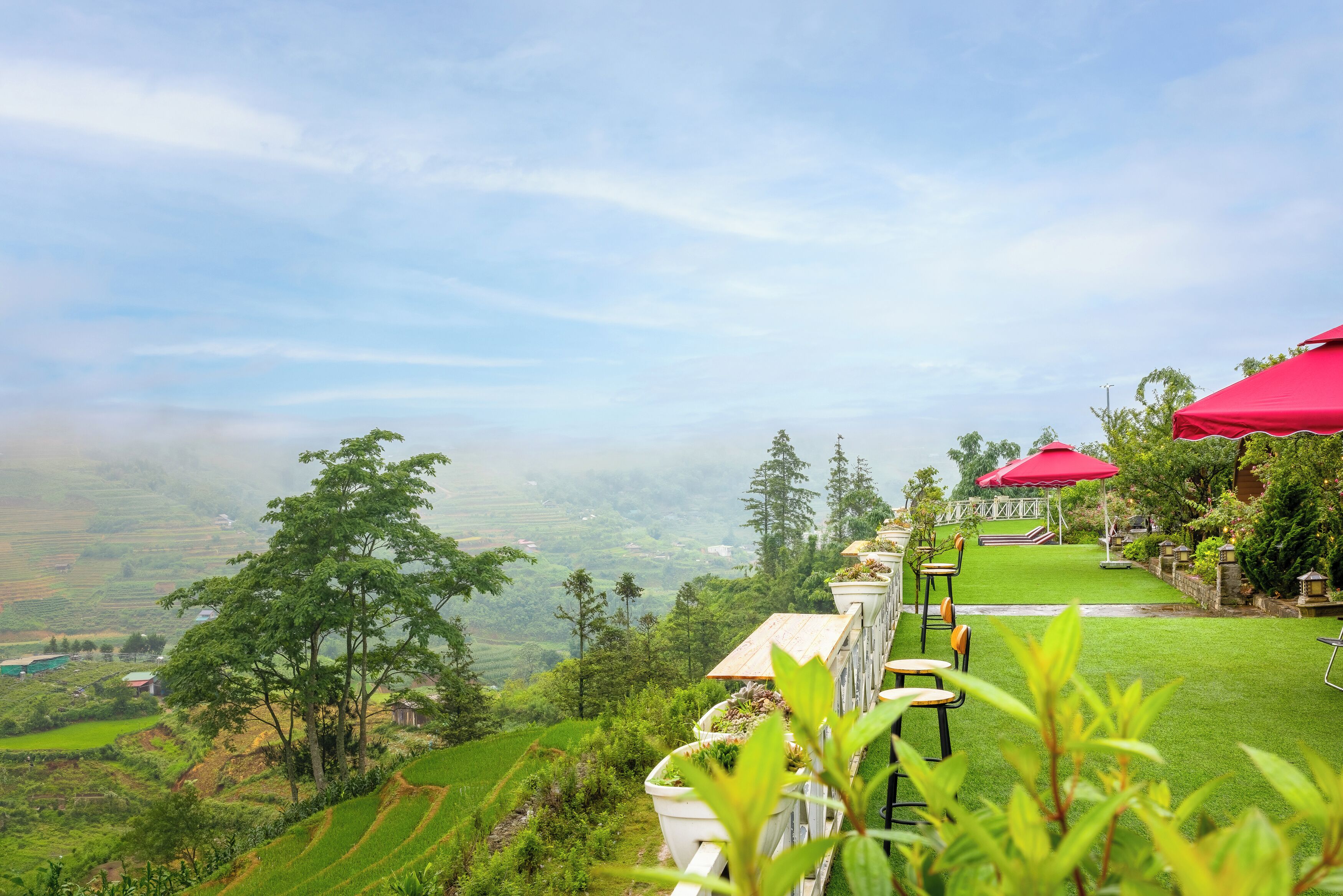 A terrace with a view of terraced fields, a red umbrella, and a white building with a balcony.