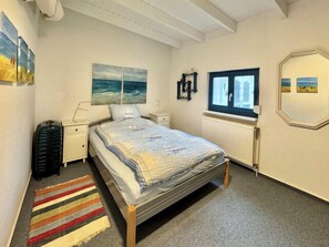 Un dormitorio con cama, ventana, radiador y cuadros en las paredes.