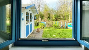 Blick aus dem Fenster auf ein kleines blau-weißes Gebäude mit einem Garten davor.