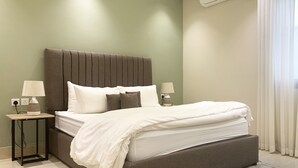 Ein ordentlich bezogenes Bett mit weißer Bettwäsche, einem braunen Polsterkopfstück und zwei Nachttischen mit Lampen.