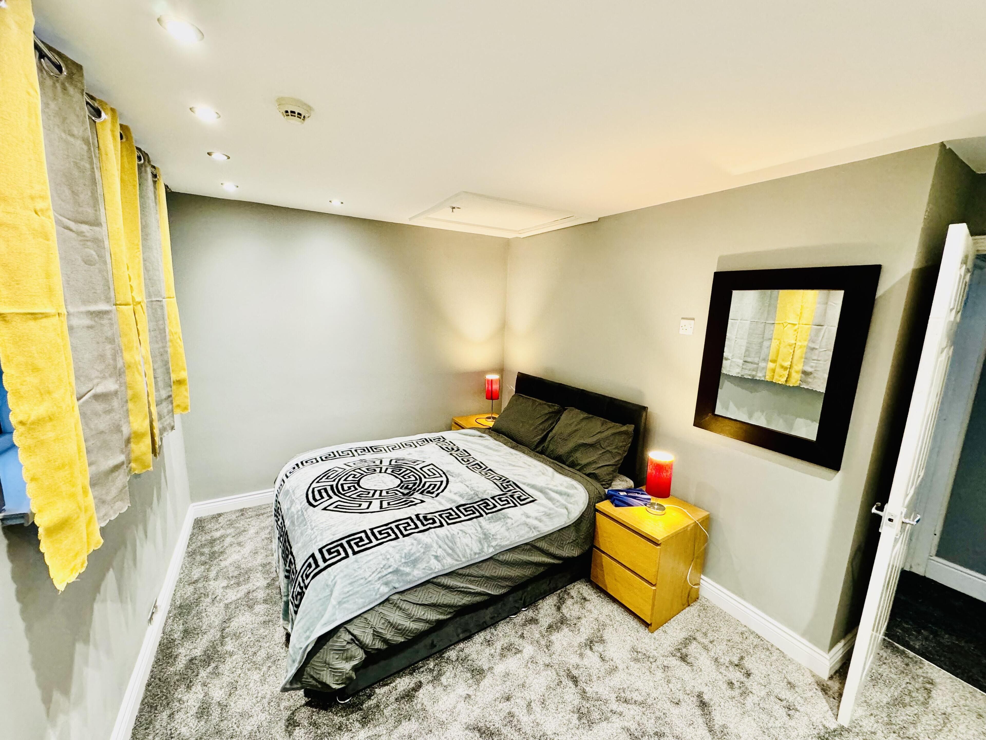 A bedroom with a bed, two bedside tables, a nightstand, a mirror, and a door.