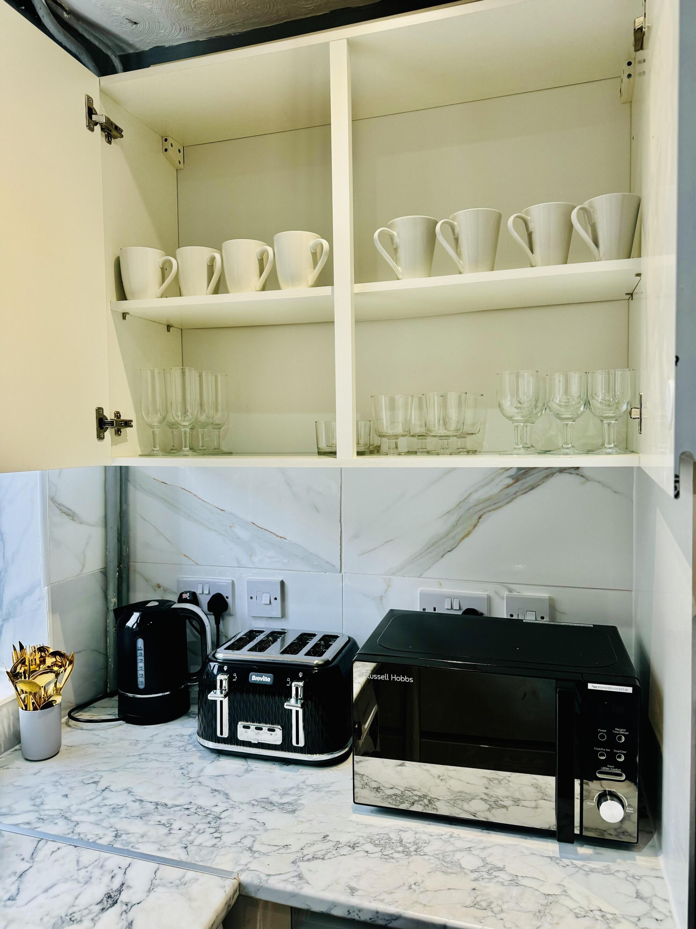 Una cocina con armarios blancos, encimera de mármol, tostadora, hervidor y microondas.