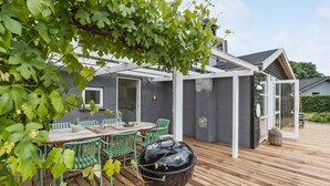 A covered patio with a wooden deck, a grill, and a table with chairs. - Lovely home in Knebel with kitchen (Knebel)