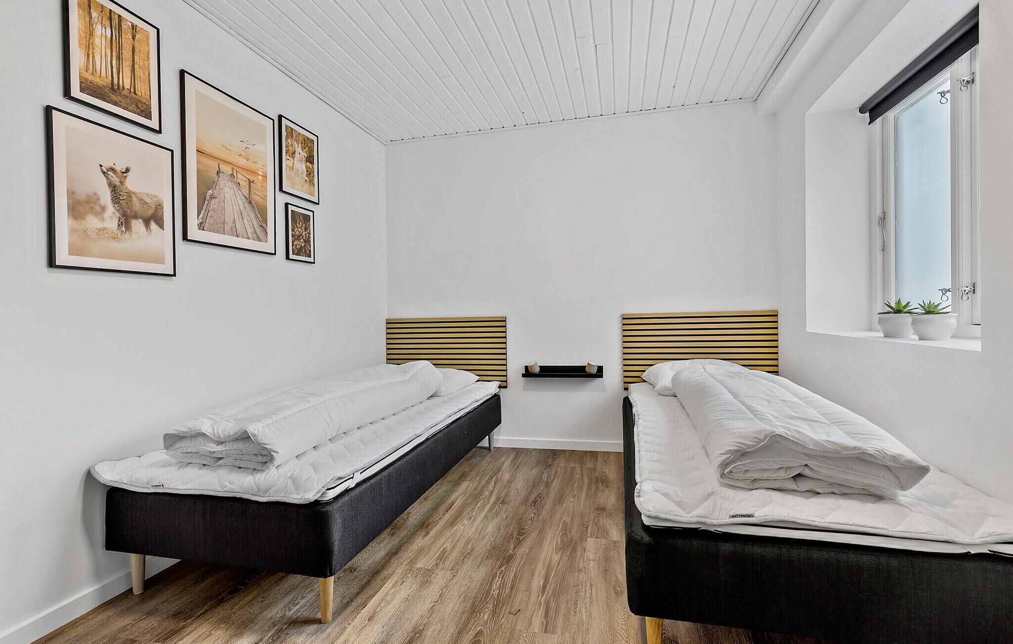 Una camera da letto con due letti, pavimento in legno e una finestra con piante.