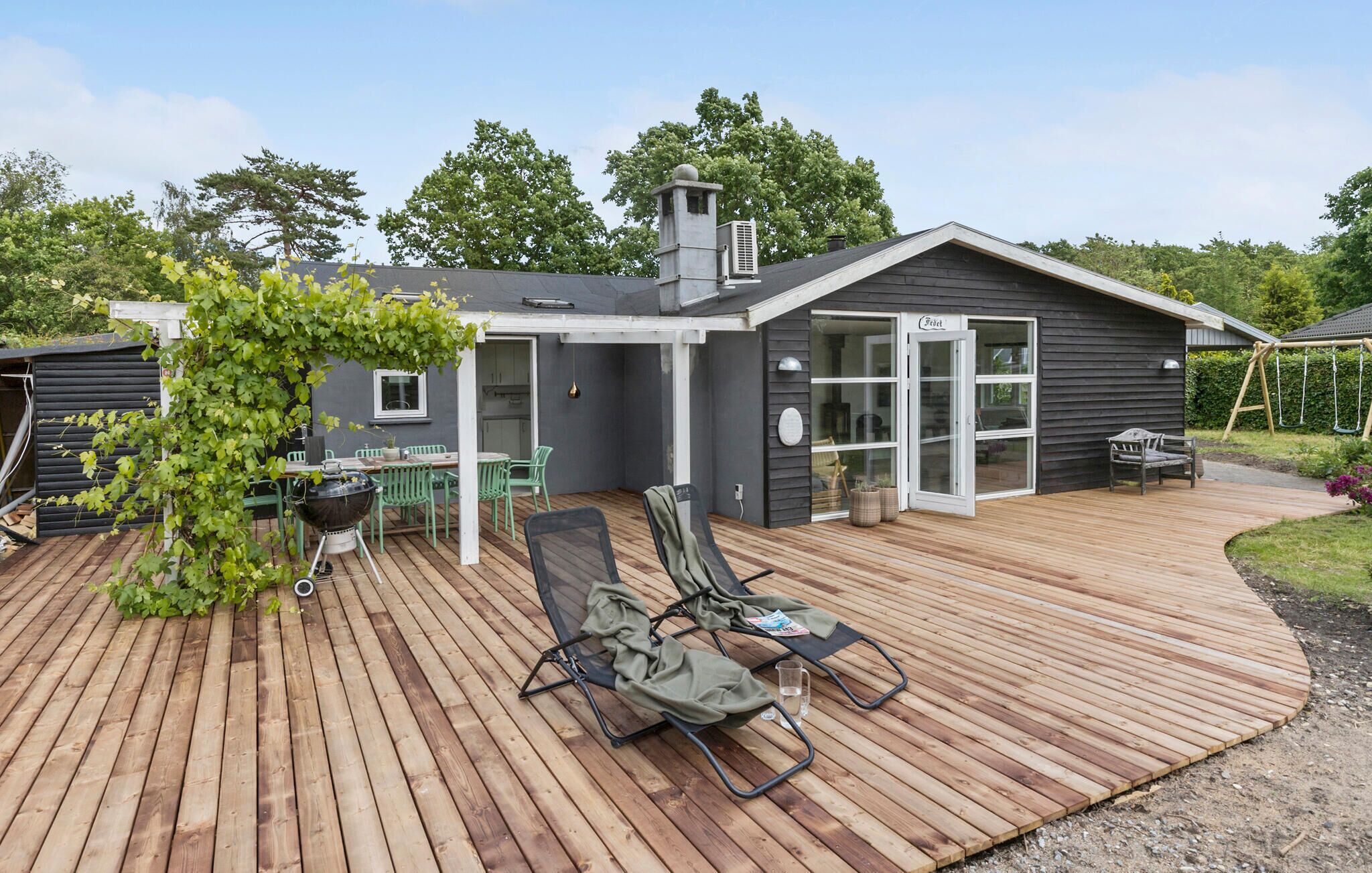 A modern house with a wooden deck, a covered patio, a grill, and a swing set.