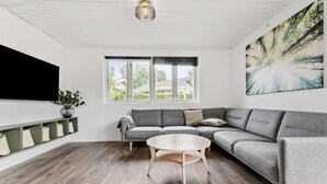 A modern living room with a grey sectional sofa, a round coffee table, and a large window with a view of greenery outside. - Lovely home in Knebel with kitchen (Knebel)