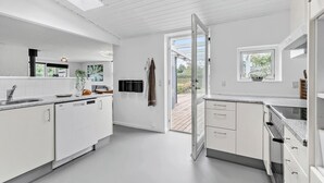 A modern kitchen with white cabinetry, a built-in dishwasher, and a large window overlooking a wooden deck. - Lovely home in Knebel with kitchen (Knebel)
