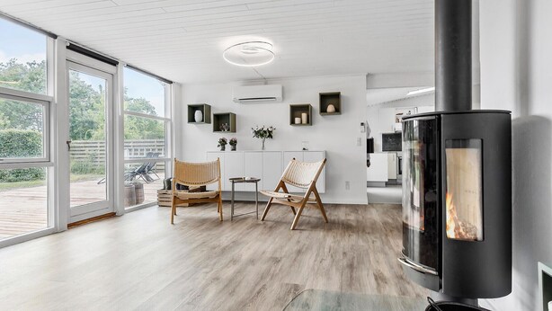 A modern kitchen with a large stove, wooden flooring, and a dining area with wicker chairs. - Lovely home in Knebel with kitchen (Knebel)