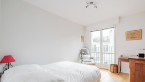 Un dormitorio con una cama, una silla, una mesa de madera y una ventana.
