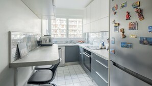 Una cocina moderna con comedor, que incluye un refrigerador con imanes, una ventana con vista a edificios y un salpicadero de azulejos.
