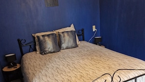 Un dormitorio con cama, mesita de noche, lámpara y un adorno en la pared.