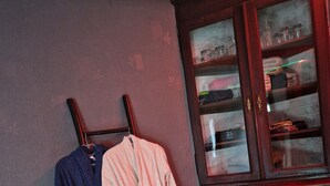 Un baño con un mueble de madera, un perchero con dos batas y piso de baldosas.