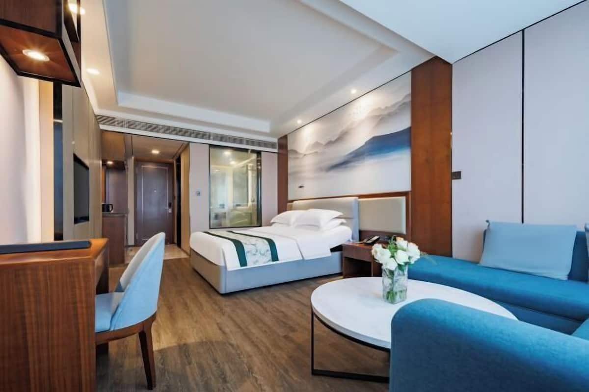 A modern hotel room with a bed, a sofa, a dining table, and a wall-mounted TV.