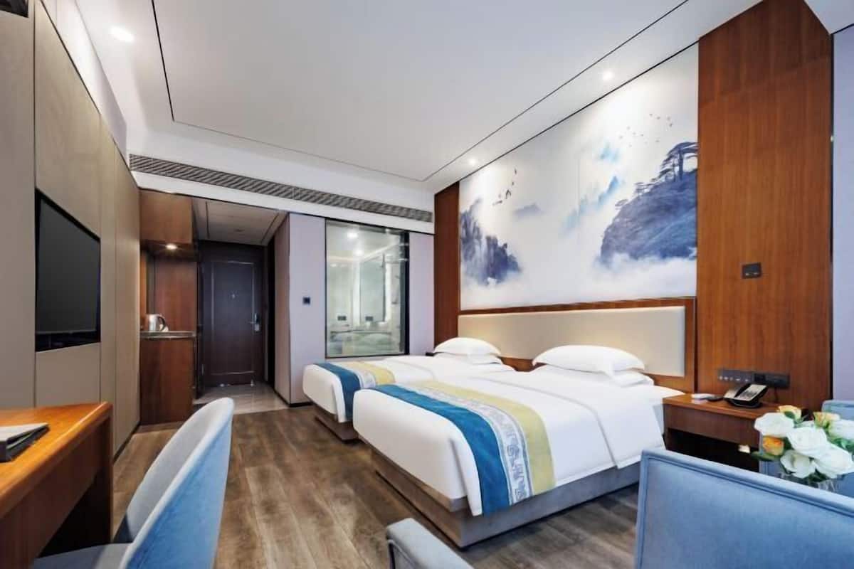 A hotel room with a bed, bedside table, chair, desk, and a large window.