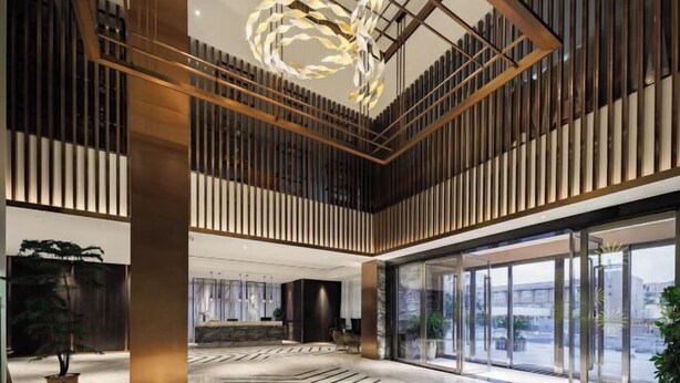 A spacious lobby with a high ceiling, modern lighting, and large windows offering views of the city. - Dingshang Hotel (Wuxi)