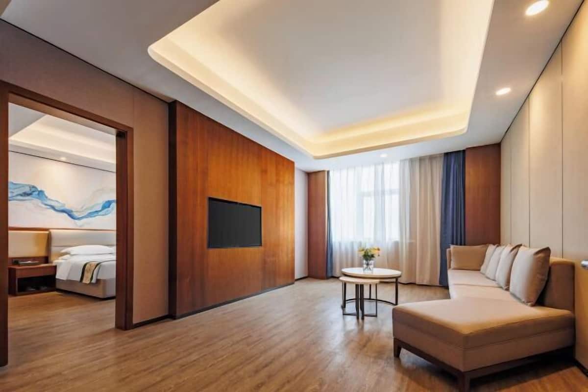 A modern hotel room with a wooden floor, a sofa, a bed, a TV, and a painting on the wall.