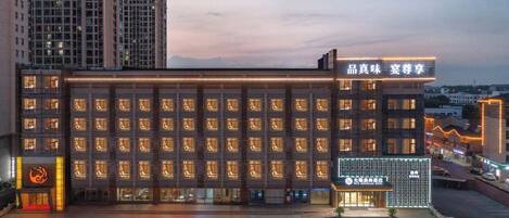 A hotel with a modern facade, multiple floors, and a parking lot in front.