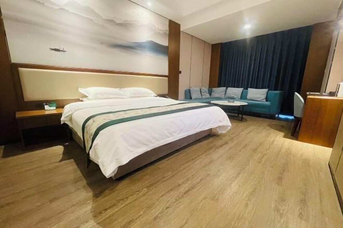 Habitación de hotel con una cama grande, un sofá, una mesita redonda y vistas al exterior.