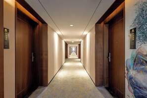 A hotel hallway with wooden doors, a patterned carpet, and a wall with a floral mural. - Dingshang Hotel (Wuxi)