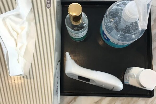 Una bandeja negra con una caja de pañuelos blancos, un dispensador de gel antibacterial, una botella de agua y un cepillo de dientes eléctrico blanco.