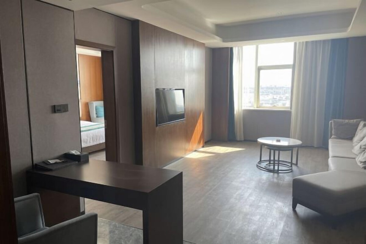 Una habitación de hotel moderna con una cama, un escritorio, un televisor, una mesa de centro redonda y un sofá.